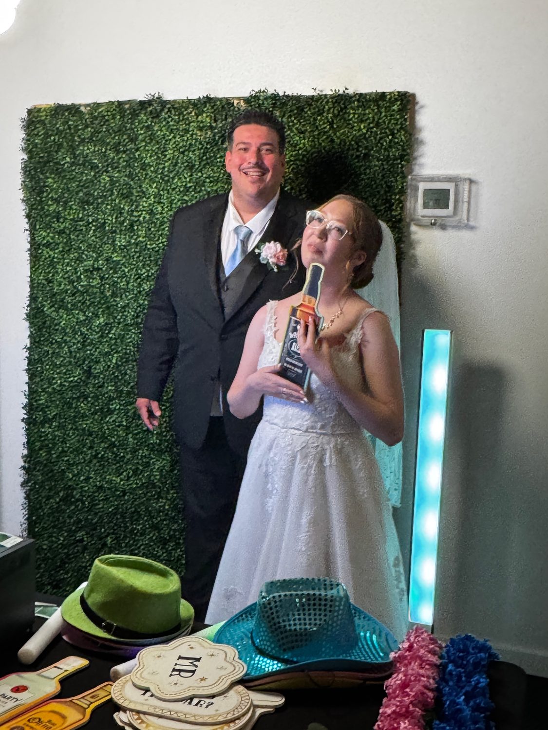 A couple at the photo booth in front of a greenery wall